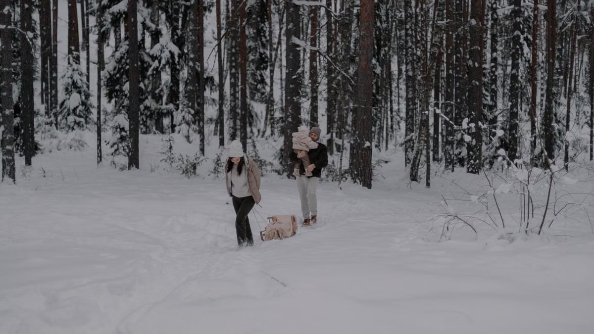 A couple enjoys a winter walk with their dog in a snowy forest path.