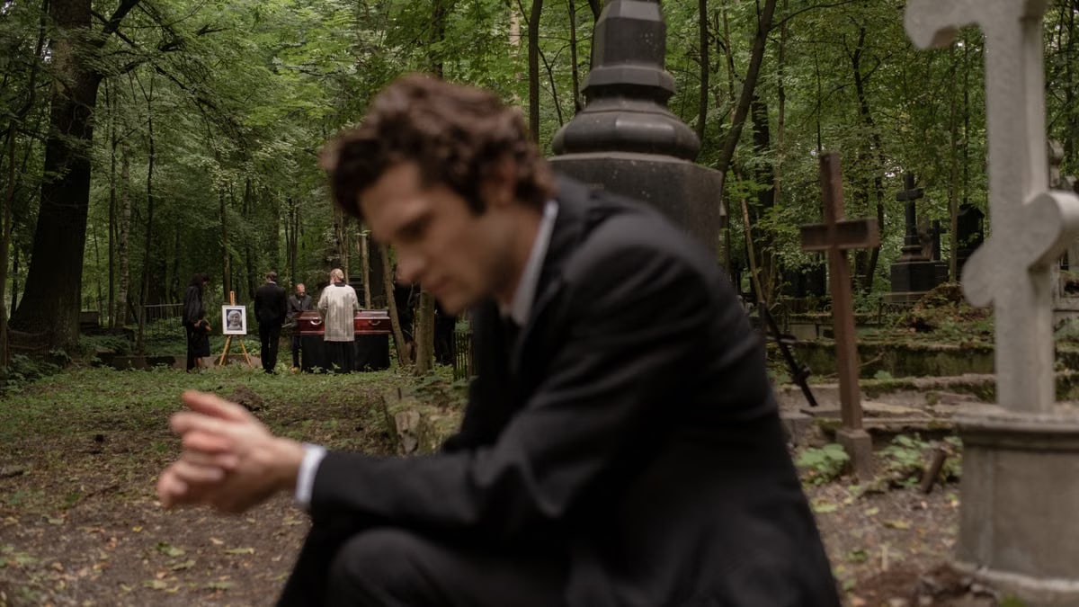 A man in mourning at a funeral surrounded by gravestones in a serene forest cemetery.